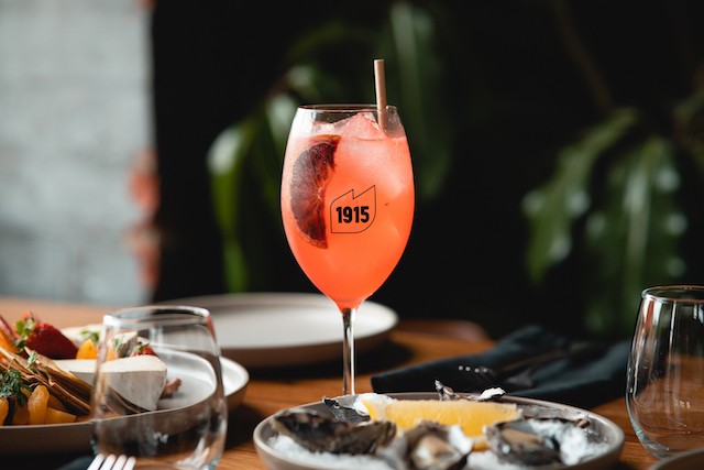 showing a cocktail in a branded 1915 cocktail glass with a meal